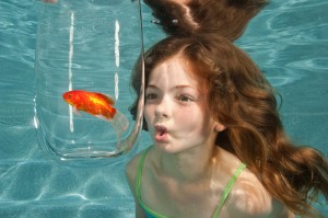 swimming underwater in swimming pool looking at goldfish in glass bowl