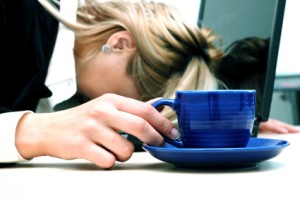 Tired woman are sleeping and holding cup. Laptop is situated on the table.