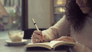 videoblocks young beautiful woman writing on her diary and drinking cappuccino in a cafe bu0yfgxjx thumbnail full01